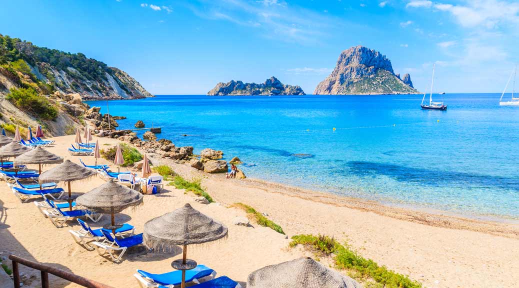  Cala d'Hort beach with sunbeds and umbrellas and beautiful azure blue sea water, Ibiza island, Spain