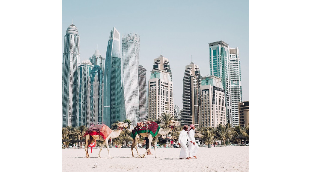 People walking on sand with camels at Dubai