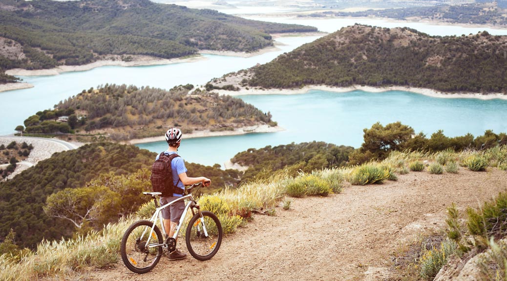 Panoramic view of cyclist with mountain bike enjoying beautiful mountains view.