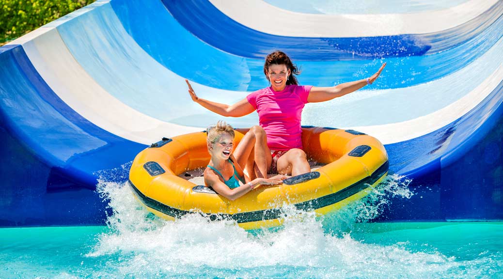 Child with mother on water slide at aquapark.