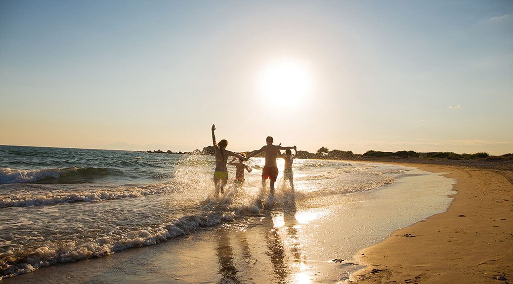 Family with two children running through the sea water on the beach during sunset