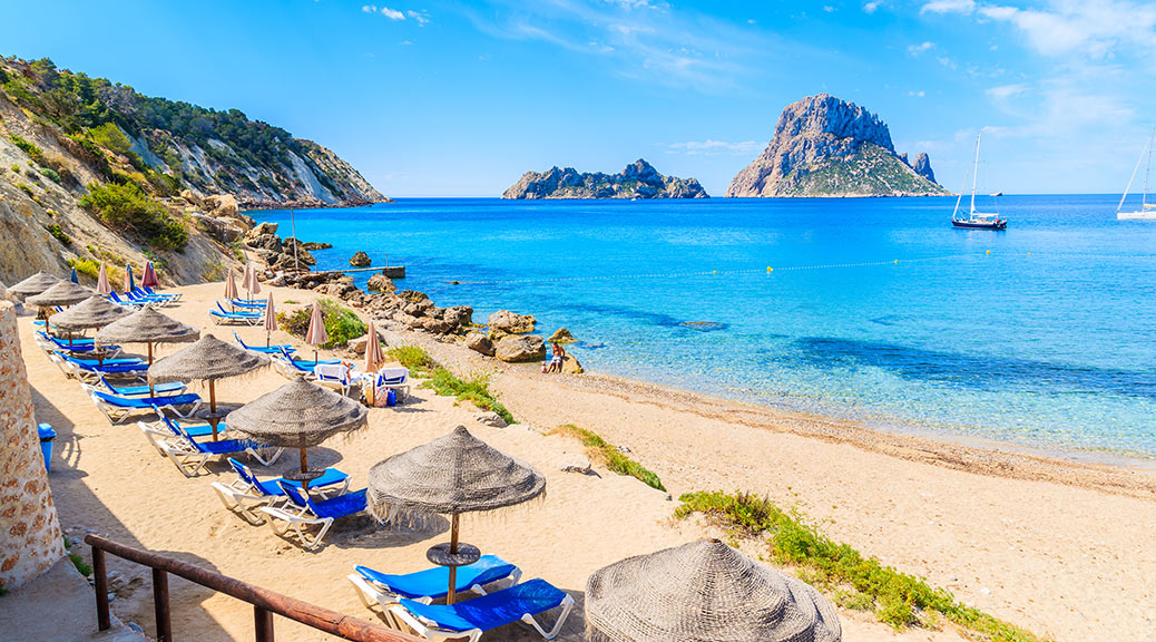  Cala d'Hort beach with sunbeds and umbrellas and beautiful azure blue sea water, Ibiza island, Spain