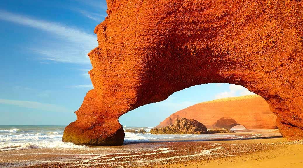 Amazing red rock arch on the golden sand beach of Morocco