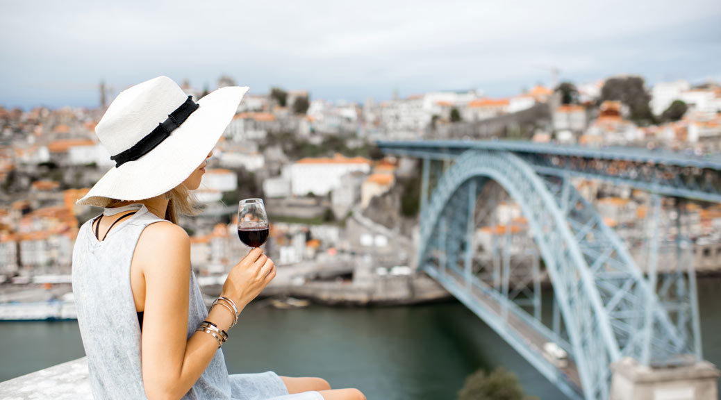 Young woman tourist sitting with glass of Porto wine on the terrace with great cityscape view on Porto city in Portugal