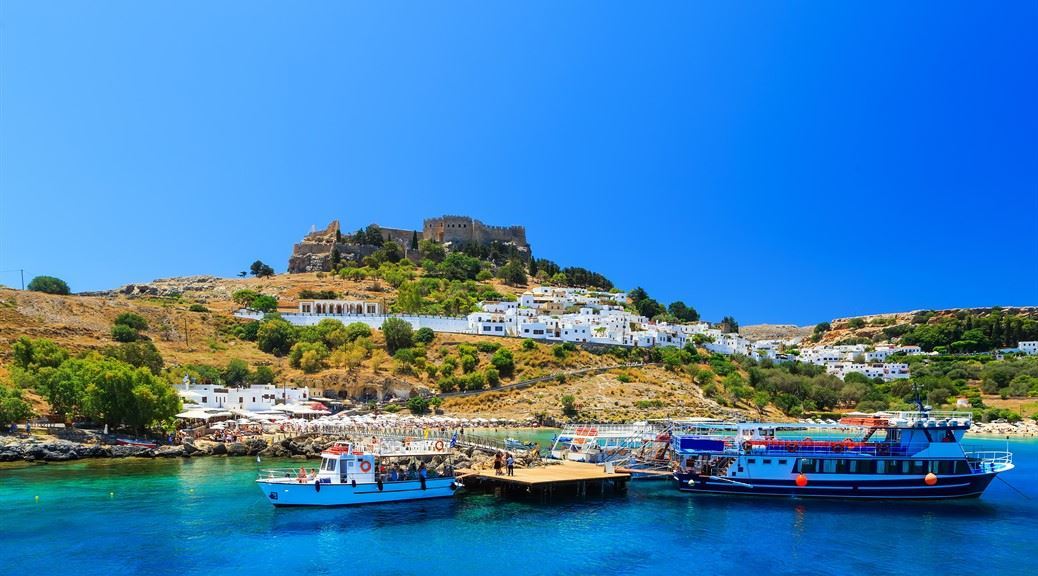 Boats and cruises at the port of the town of Lindos sea bay and fort ruin seen at the top of the island