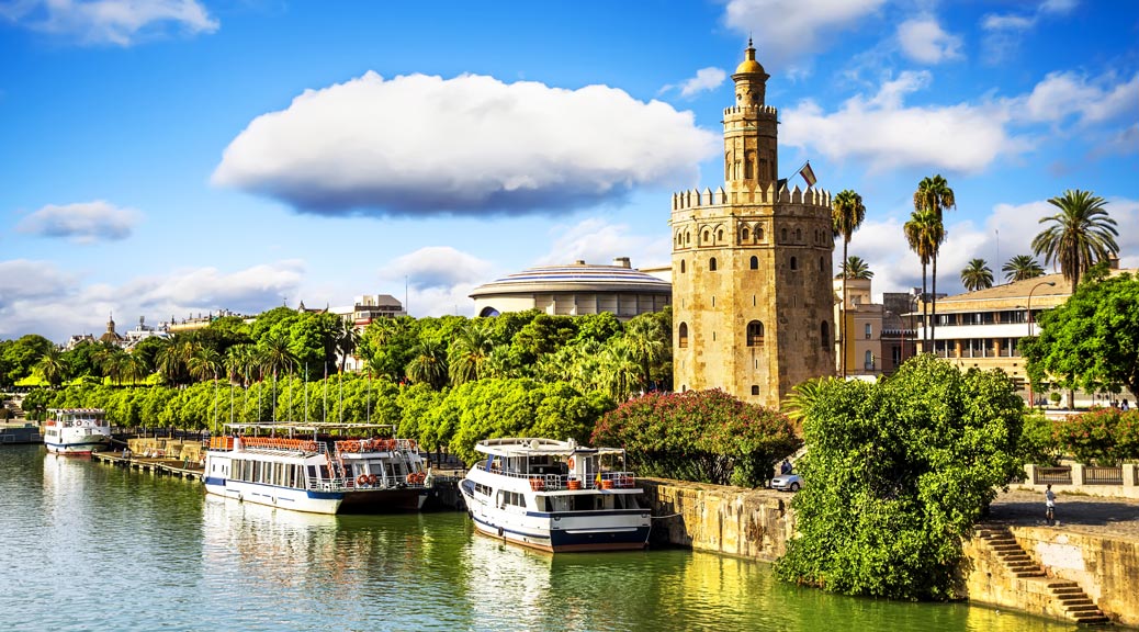 Golden tower in Seville with trees and boats with blue sky, Andalusia, Spain.