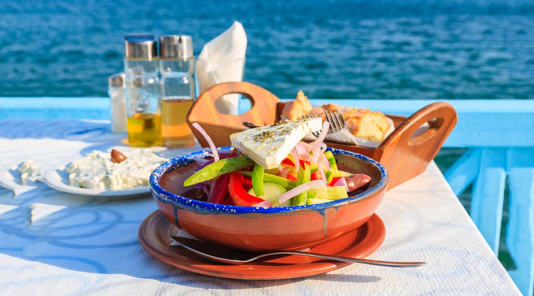 Greek salad on table in Greek tavern with blue sea water in background, Samos island, Greece