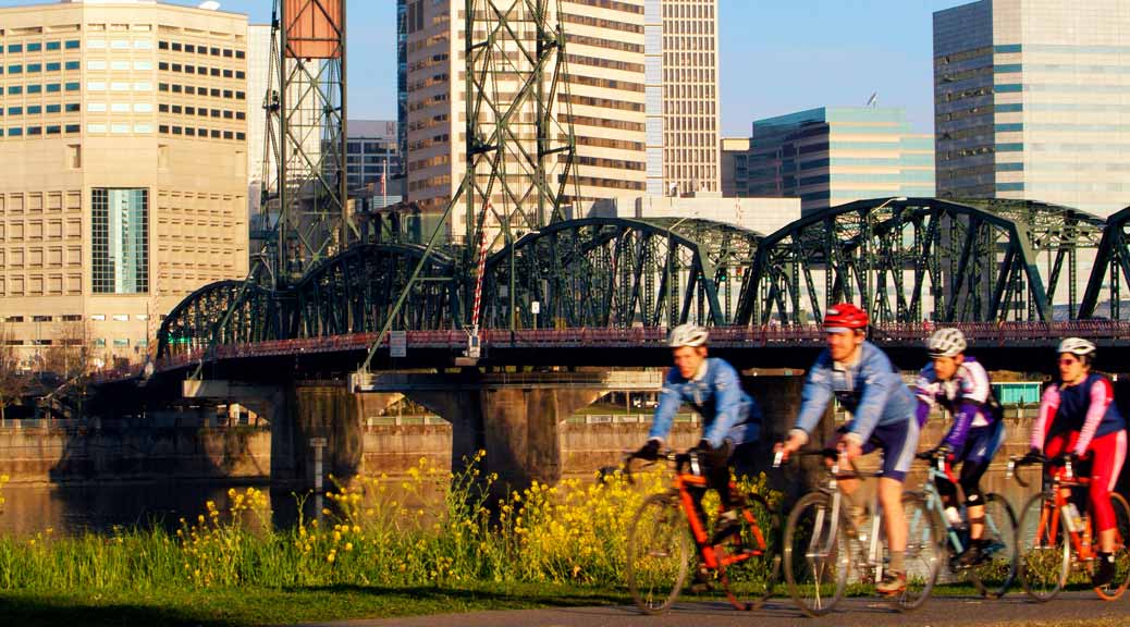 bikers riding along the eastside esplanade in portland while hawthorne bridge is in the background