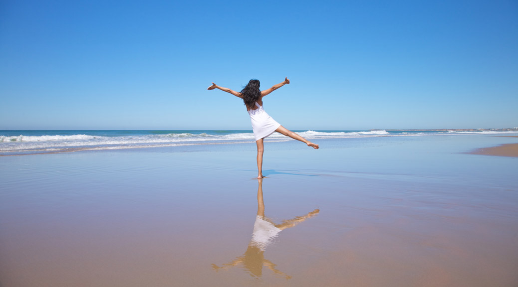 Girl jumping on the beach with reflection on the sand