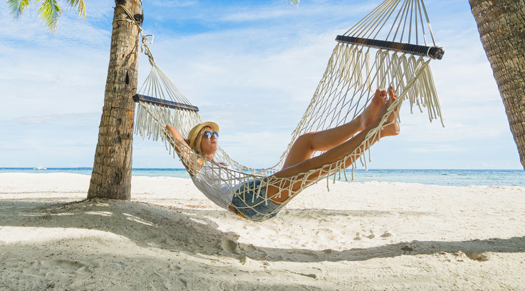 Woman in hat relaxing on hammock on the beach
