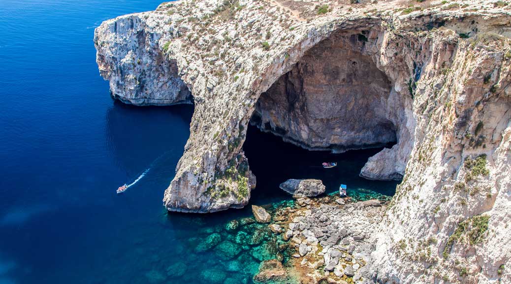 Boats on a clear blue sea water under Grotto grey rock cave formation 