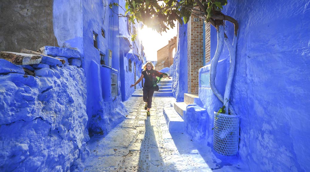 Happy girl walking on the blue streets of Chefchaouen, Morocco.