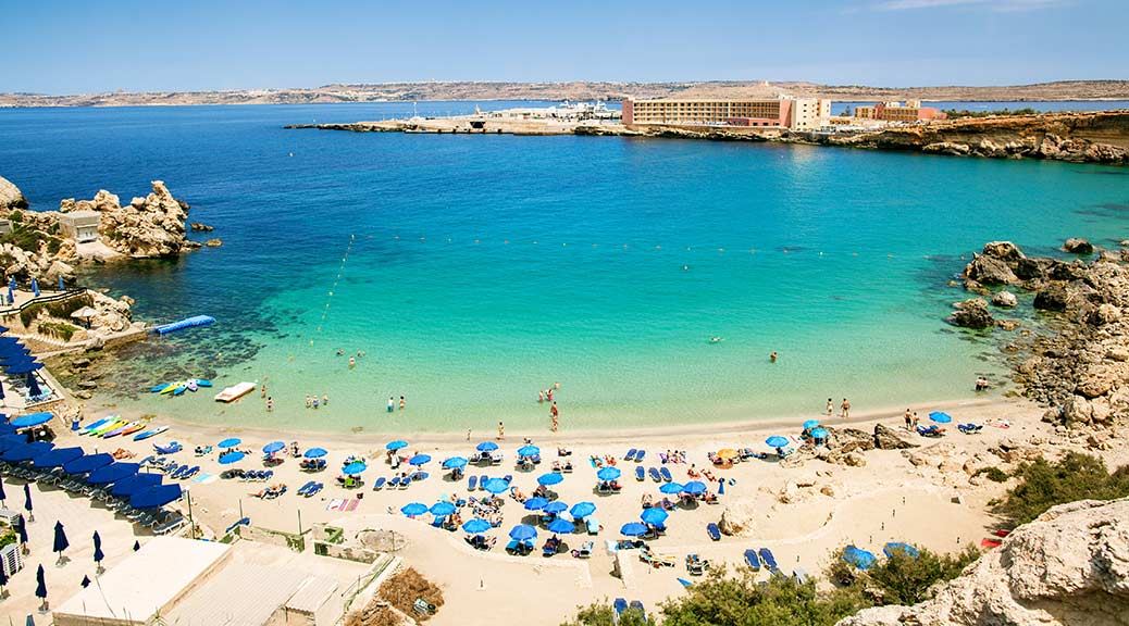 Blue umbrellas on tropical beach with white sand turquoise sea water in Malta
