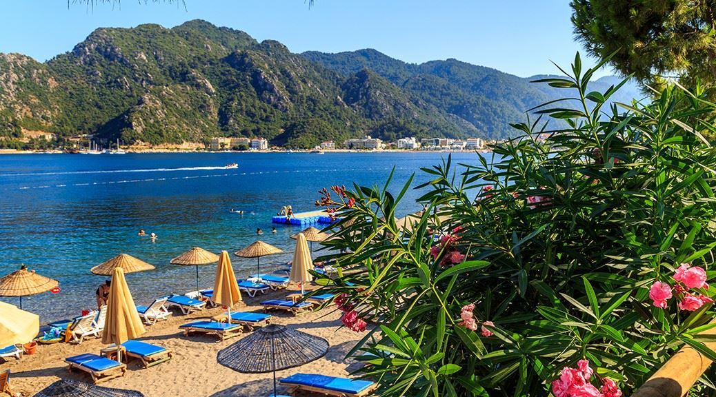 mountains seen beyond the sea through marmaris beach with sunbeds and umbrellas